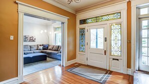 A spacious living room with a sectional sofa, a chandelier, and a stained glass door. - Queen Ann Historic Mansion (Covington)