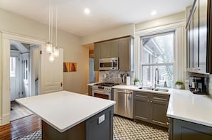 A modern kitchen with a central island, stainless steel appliances, and a large window providing natural light. - Queen Ann Historic Mansion (Covington)