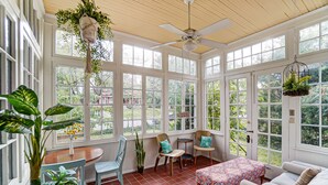 A sunroom with large windows, a ceiling fan, and a dining area with chairs and a table. - Queen Ann Historic Mansion (Covington)