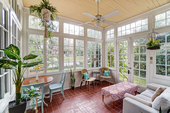 A sunroom with large windows, a ceiling fan, and a dining area with chairs and a table. - Queen Ann Historic Mansion (Covington)