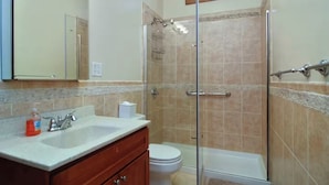 Un bagno con doccia vetrata, un water bianco, un lavandino con specchio e un armadietto in legno.