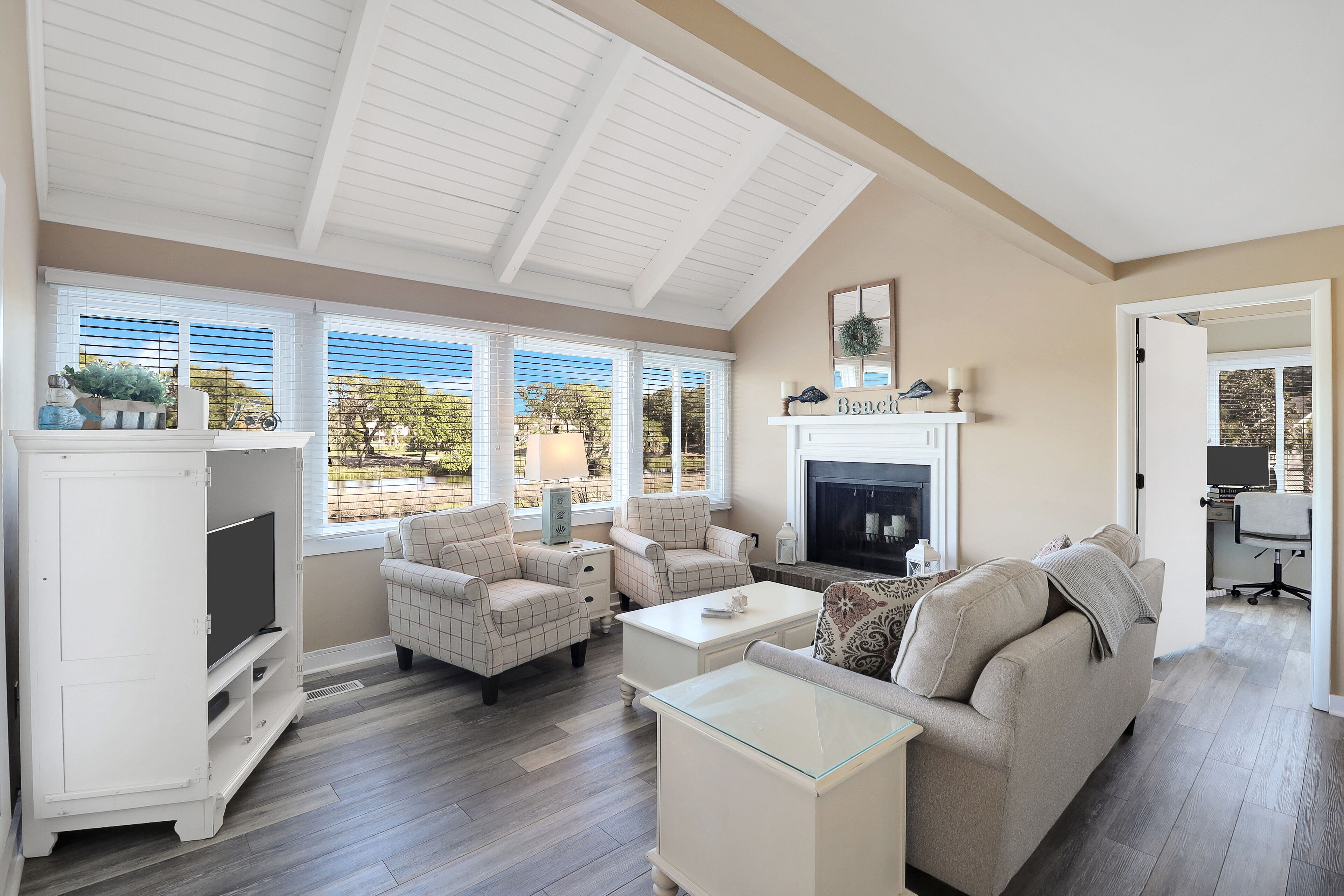 A spacious living room with a high ceiling, large windows, a fireplace, and a television.