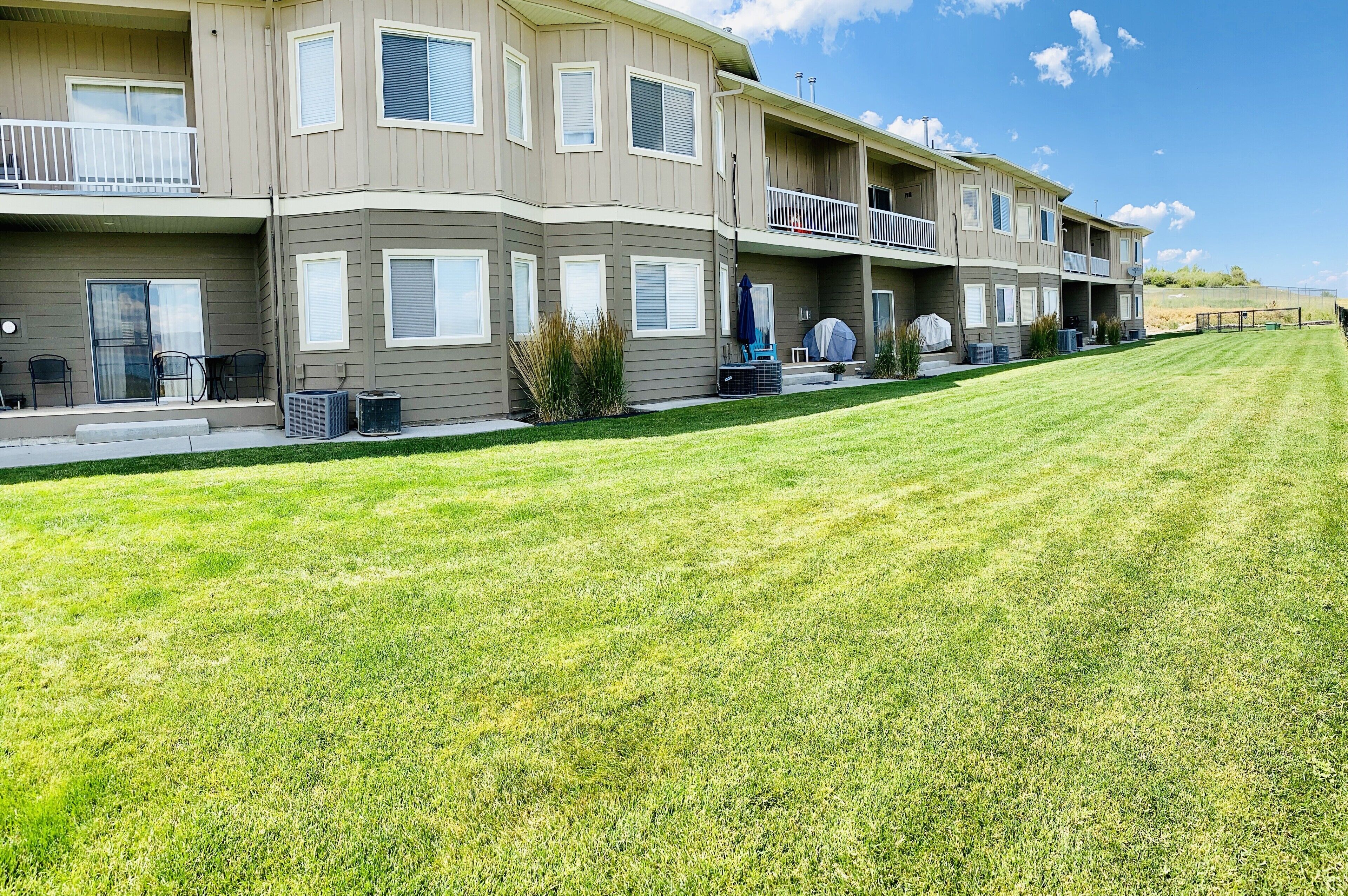 A multi-story apartment building with balconies, outdoor seating, and a well-maintained lawn.