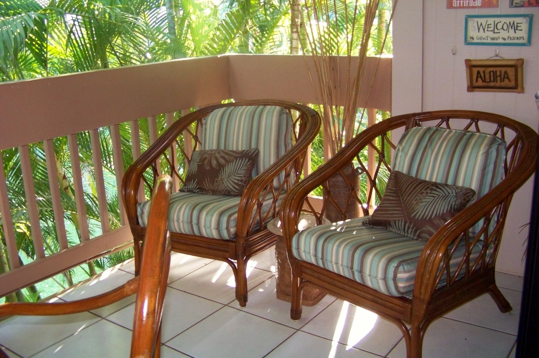 Two wicker chairs with striped cushions on a balcony with a view of tropical foliage.