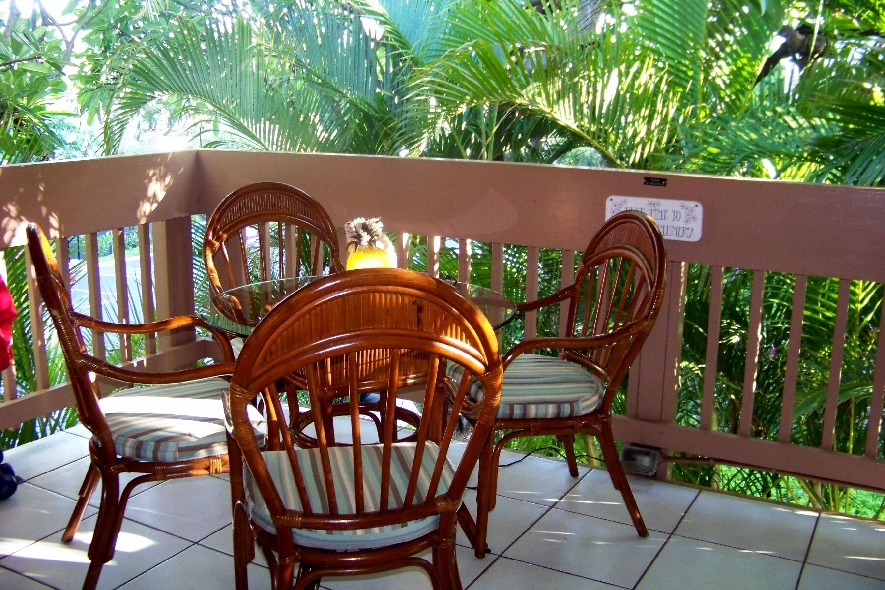 Un balcone con sedie in vimini e un tavolo, immerso in una rigogliosa vegetazione.