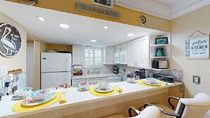 Cucina con mobili bianchi, un frigorifero e un'area pranzo con un sottopiattino giallo.
