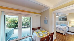 Una stanza con un tavolo da pranzo apparecchiato per quattro persone, un letto con copriletto a righe, un comodino e una sveglia a parete.