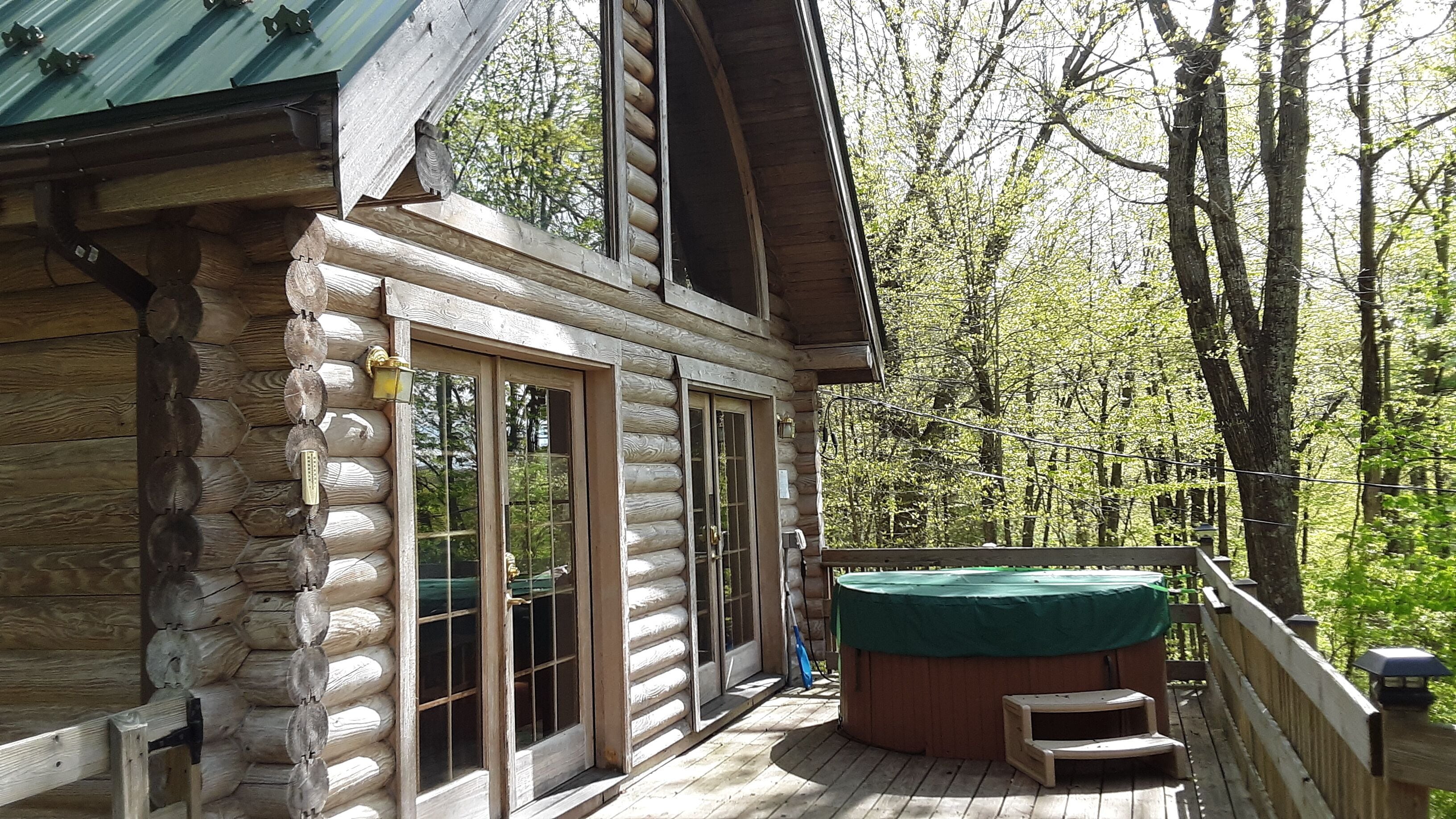 Eine Blockhütte mit einer Terrasse, großen Fenstern und einem Whirlpool.