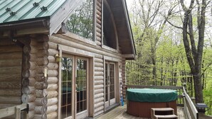 Une cabane en rondins avec une terrasse, de grandes portes vitrées et un jacuzzi.