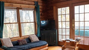 L’intérieur d’une cabane en rondins, avec un lit en bois, un téléviseur et une table à manger.