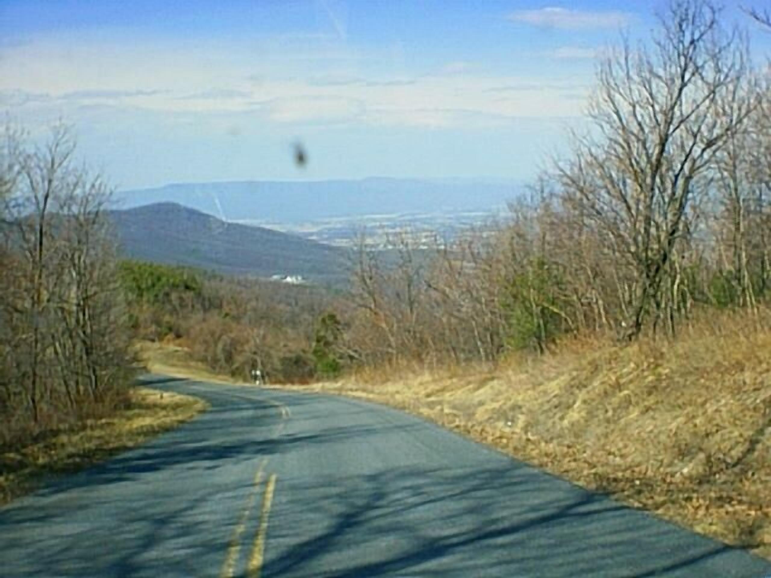A rural road with a clear view of distant mountains and sparse vegetation.