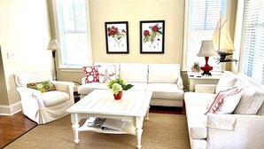 A living room with a white sofa, a white coffee table, and two framed floral paintings on the wall. - Designer Saltmarsh Townhome! Neighborhood Pool! Great Location! Amenity access included! (Seabrook Island)