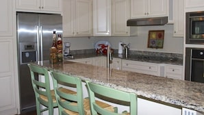 A kitchen with white cabinets, a stainless steel refrigerator, a granite countertop, and two green chairs. - Designer Saltmarsh Townhome! Neighborhood Pool! Great Location! Amenity access included! (Seabrook Island)