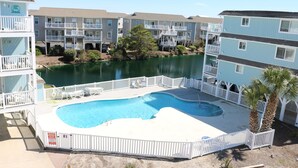 A swimming pool surrounded by a white fence, with a view of multi-story buildings in the background. - Monkey Sea, Monkey Dune ~ Top floor, End unit; Sound and Ocean view (Ocean Isle Beach)