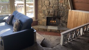 A stone fireplace with a ceiling fan, a blue sofa with cushions, and a view of a wooden deck outside. - Free Arcade Room- Great views-1/2 Mi Ski Slopes, 3 Mi. Dwntwn (Gatlinburg)