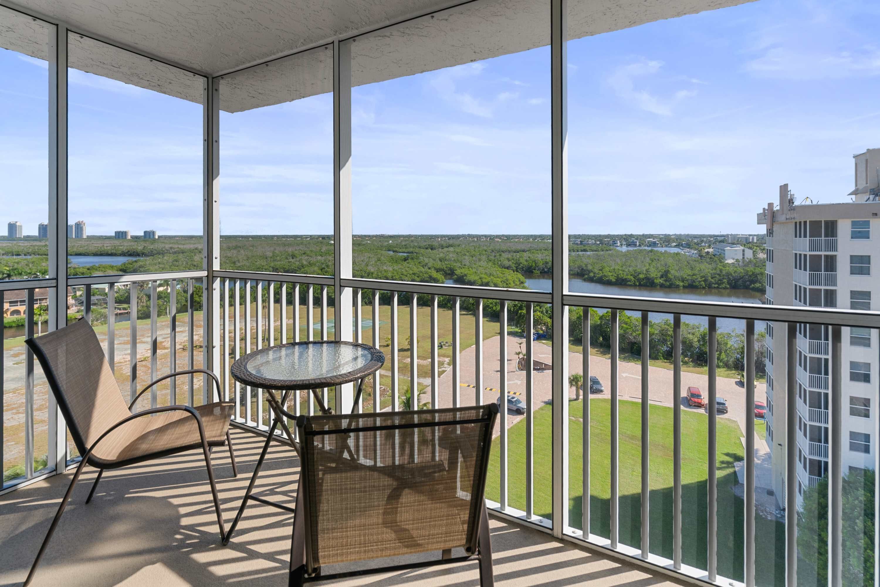 A balcony with a view of a river and greenery, furnished with two chairs and a small table.