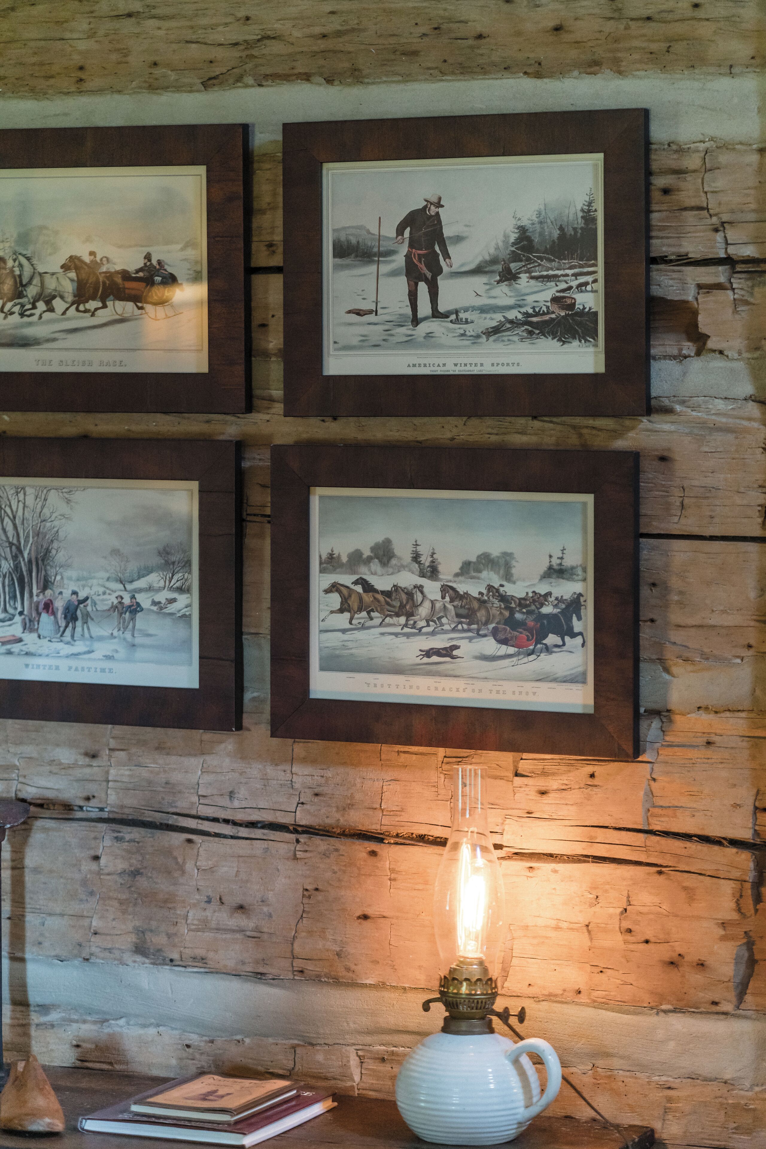 Un mur rustique orné de photographies anciennes encadrées, représentant des sports d’hiver, et d’une lampe à huile d’époque.