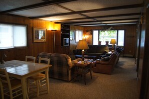 A cozy living room with a plaid sofa, a wooden dining table, and a lamp. - Cozy Cottage near sandy beach, Rainy Lake, Rainy River and Voyageur's Nat'l Park (Ranier)