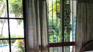 Ein Zimmer mit Bett, einem Vorhangfenster und Blick auf Pool und Grünfläche.