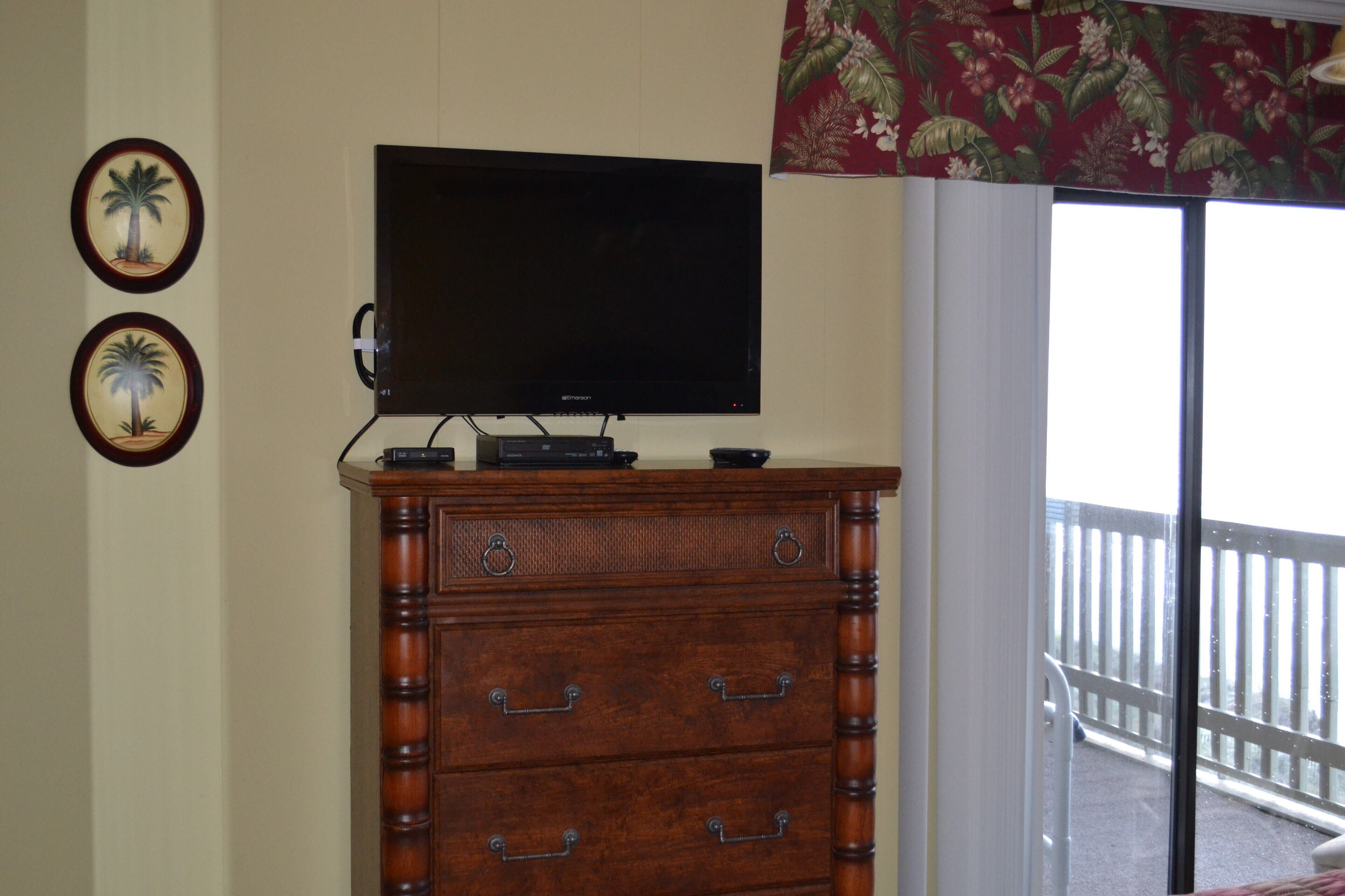 A room with a wooden dresser, a flat-screen TV on top, and two framed pictures on the wall.