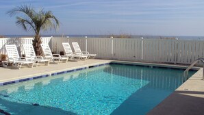 A swimming pool with clear blue water, surrounded by white lounge chairs and a palm tree.