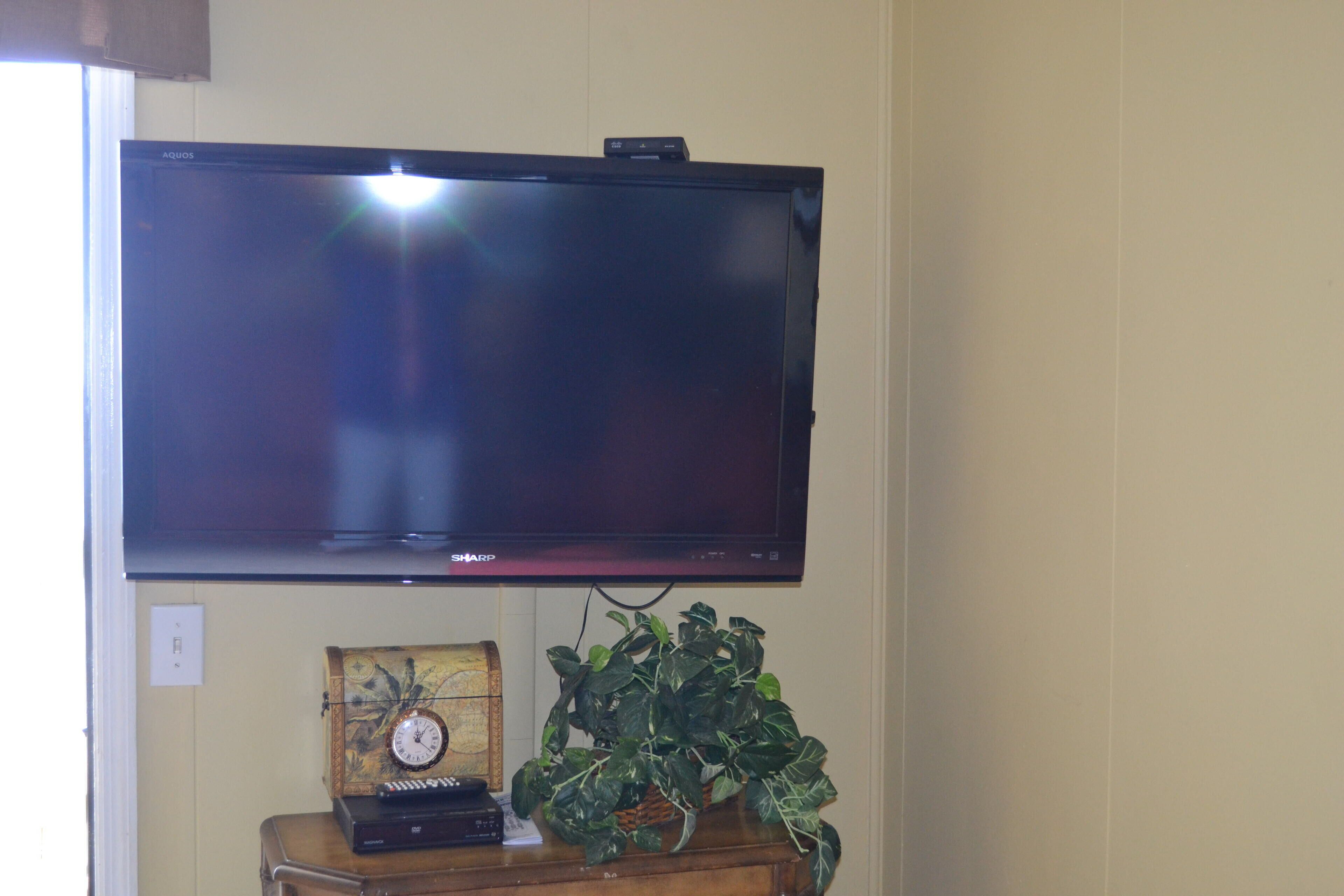 A television mounted on a wall, a wooden side table with a clock and a plant, and a power outlet.