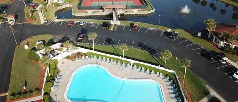 An aerial view of a resort with a large swimming pool, tennis courts, and a parking lot.