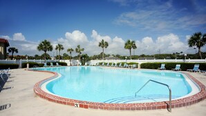 Una piscina con borde de azulejos, rodeada de sillas de descanso y palmeras.