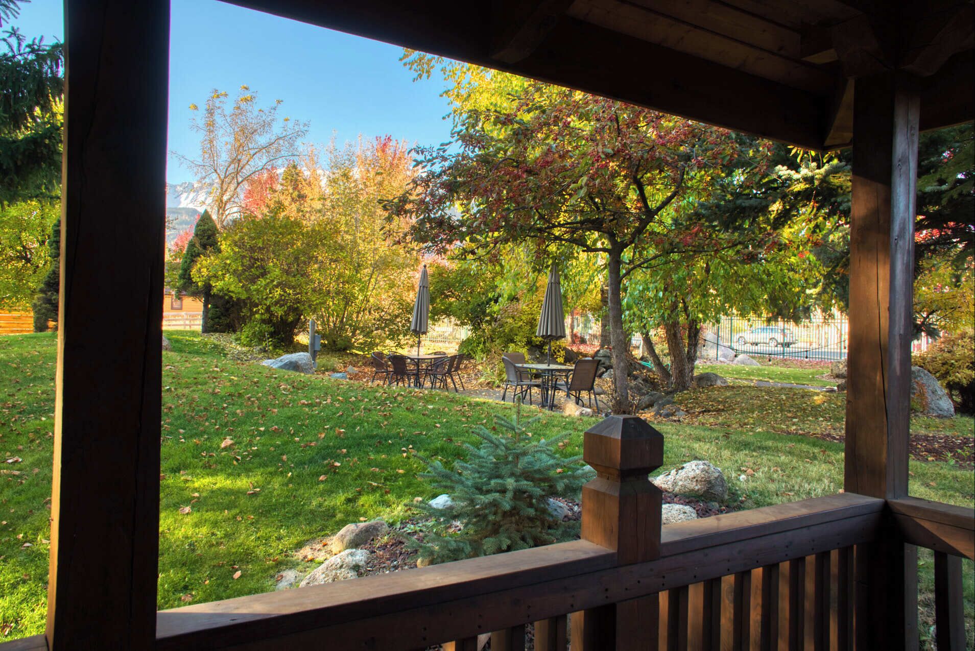 Une terrasse en bois offrant une vue sur un espace vert aménagé en parc, avec une table, des chaises et une sculpture en pierre.