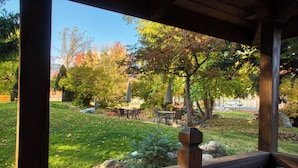 A wooden deck with a view of a park area, including a table and chairs, and a stone sculpture. - Mt. Joseph Lodge in Downtown Joseph: Unit #3 (Joseph)