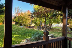 A wooden deck with a view of a park area, including a table and chairs, and a stone sculpture.