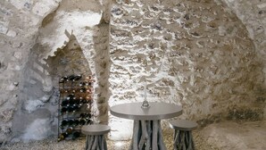 Een interieur met een rustieke stenen muur, een wijnrek en drie ronde tafels met krukken.