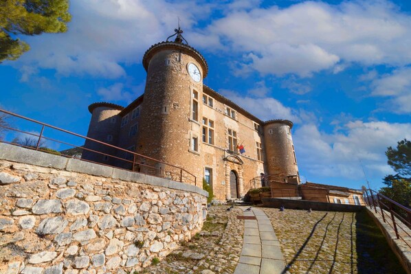 A historic stone building with a clock tower, a stone wall, and a paved pathway.