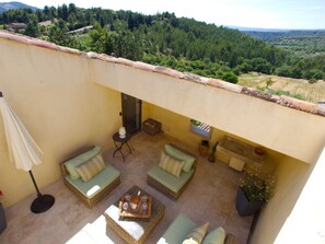 A sunlit patio with wicker furniture, a small table with drinks, and a view of a forested valley.