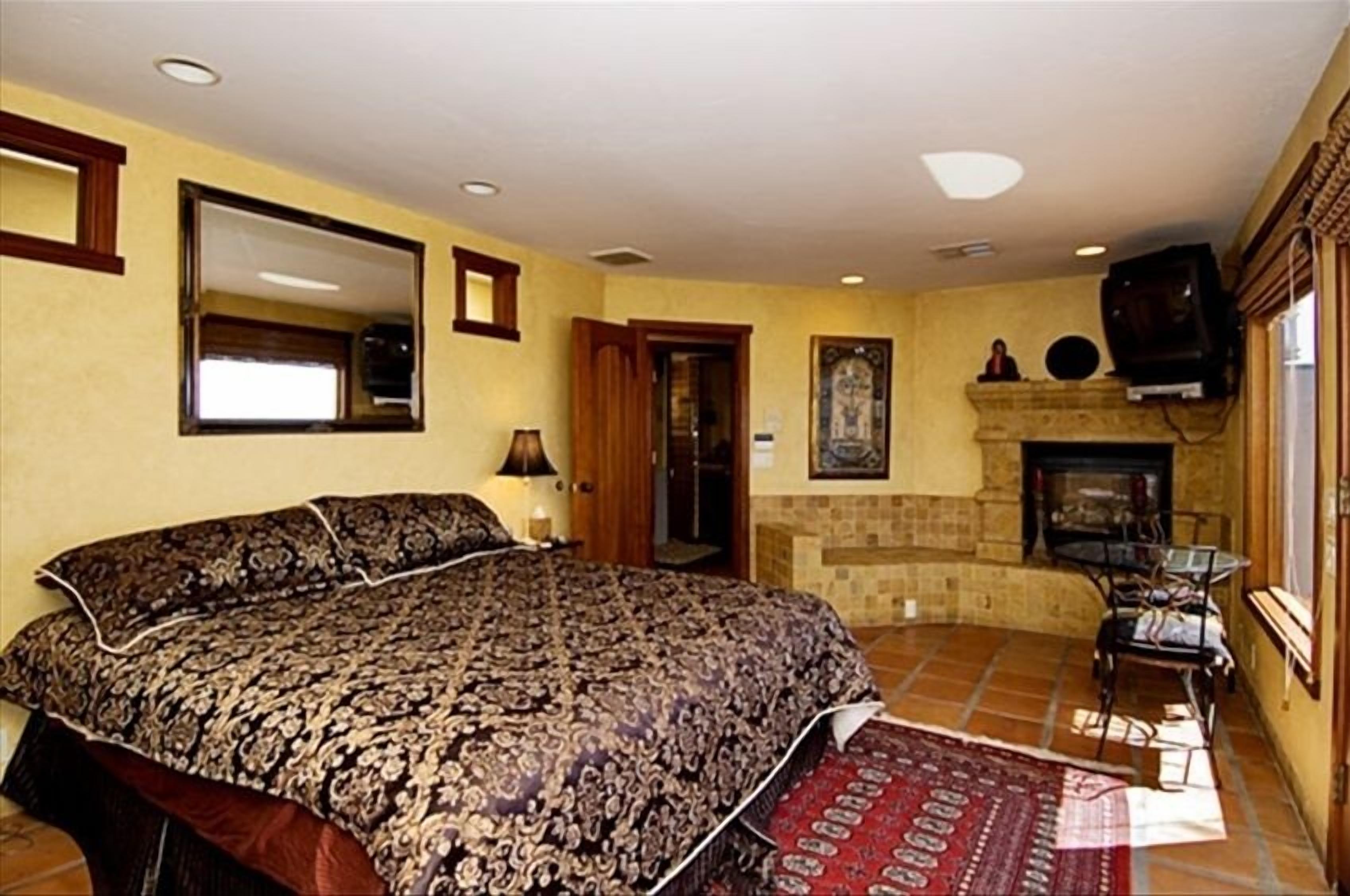 A bedroom with a large bed, a fireplace, a television, and a door leading to another room.