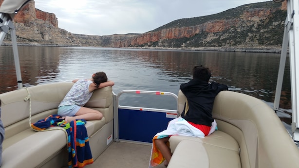 A boat with two seats, one occupied by a child and the other by an adult, with a view of cliffs and water.