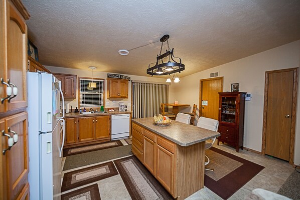 A kitchen with wooden cabinets, a white refrigerator, a central island, and a hanging light fixture.