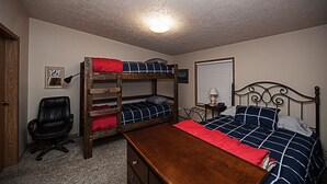 A bedroom with bunk beds, a desk, a chair, and a window with blinds.