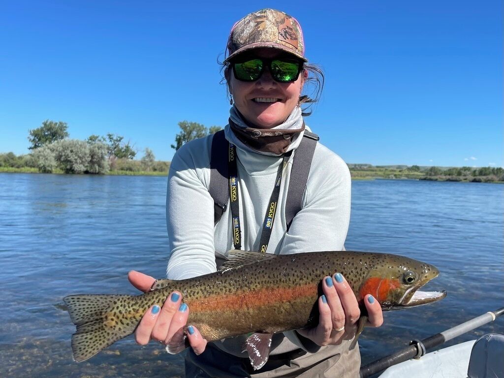 A person holding a fish by a body of water.