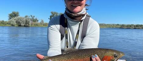 A person holding a fish by a body of water.