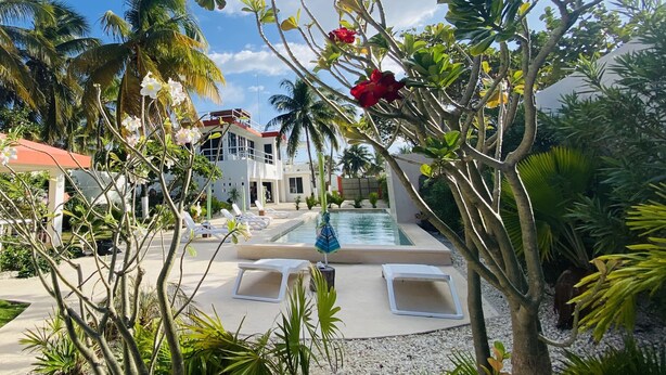 A pool area with lounge chairs, a building with a red roof, and tropical plants. - VIDA Chelem- MAR vacation property (Chelem)