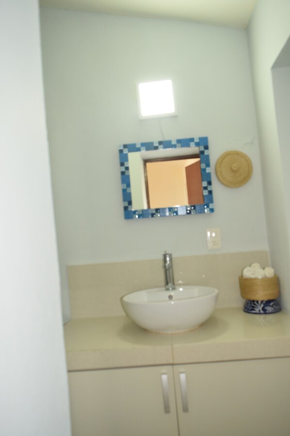 A bathroom with a white sink, a blue and white tiled mirror, and a small basket of toiletries.