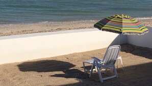 A beach chair and a colorful striped beach umbrella on a sandy beach with a view of the ocean. - VIDA Chelem- MAR vacation property (Chelem)
