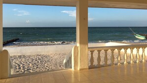 A beach view from a covered balcony with a railing, a boat on the water, and a rocky breakwater. - VIDA Chelem- MAR vacation property (Chelem)