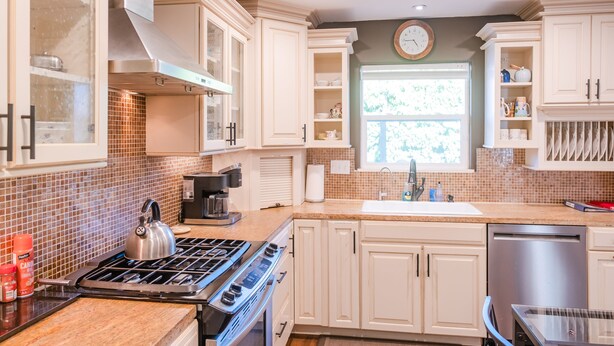 Una cocina con armarios blancos, estufa, lavavajillas y ventana con vistas a árboles.