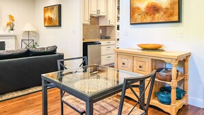 Una sala de estar moderna con una mesa de comedor de vidrio, sofá de cuero negro y un mueble de madera con electrodomésticos de cocina.