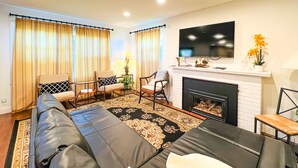 Una sala de estar con sofá, sillones, chimenea, televisor y cortinas.