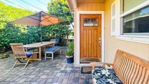 Un patio con una mesa y sillas de madera, un banco y una puerta con ventanal.