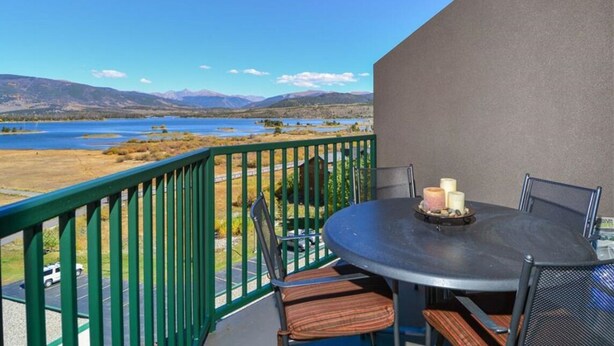 Un balcon avec une table et des chaises, donnant sur un lac et des montagnes.