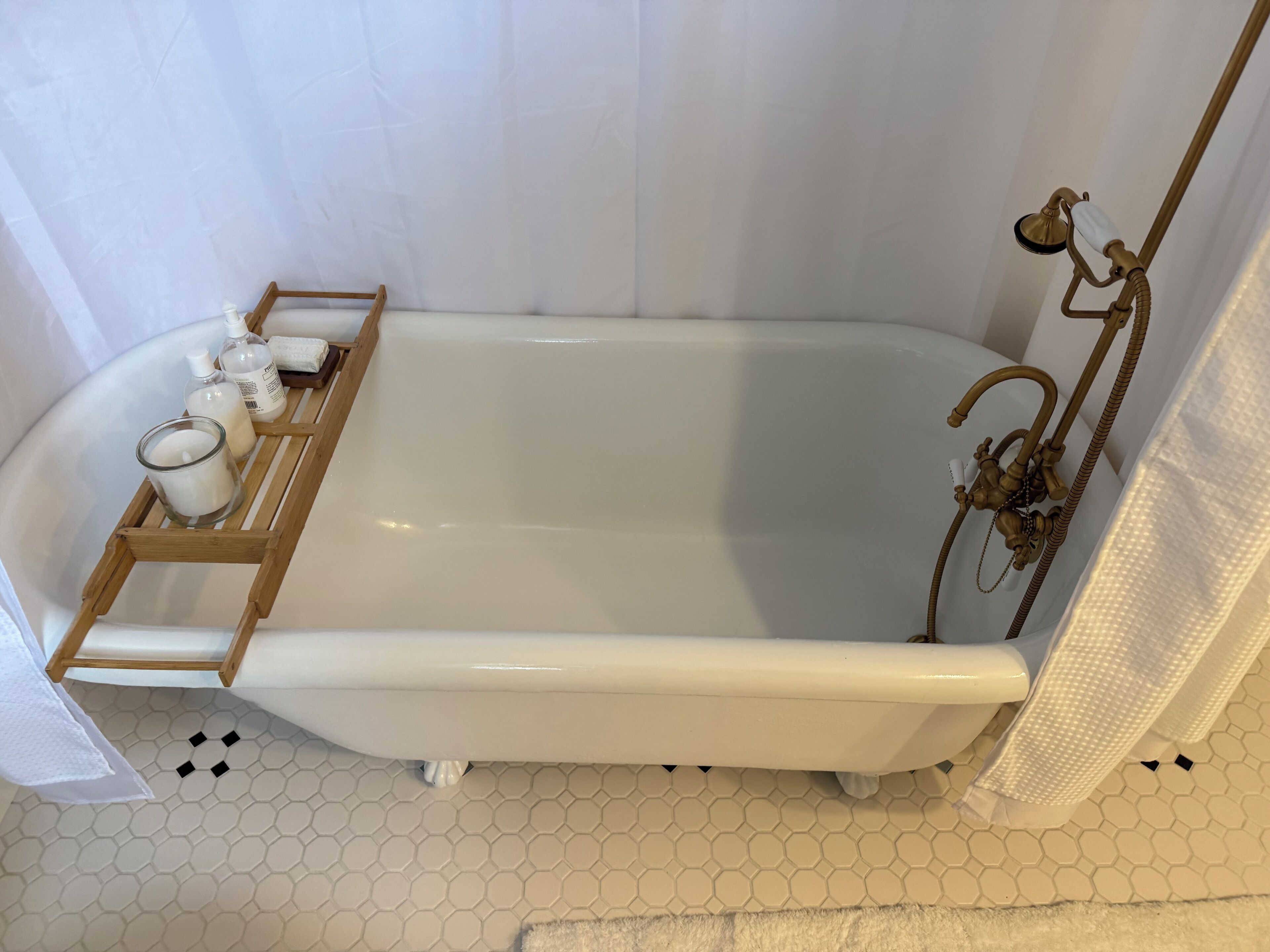 A bathtub with a wooden tray holding bottles and a candle, a showerhead, and a towel rack.